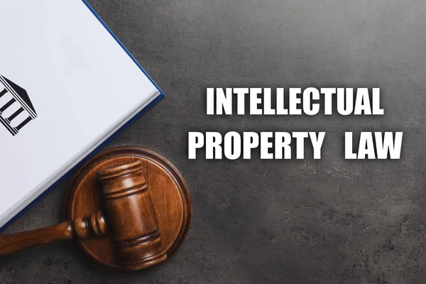 Text Intellectual Property Law, wooden judge\'s gavel and book on grey background, flat lay