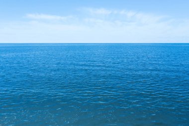 Mavi gökyüzünün altında bulutlu dalgalı bir deniz.