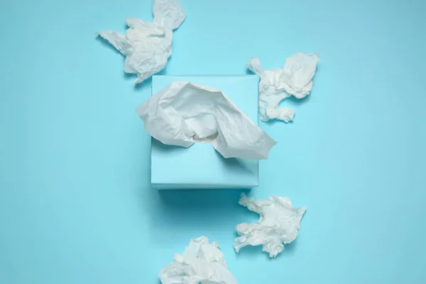 Used paper tissues and box on light blue background, flat lay