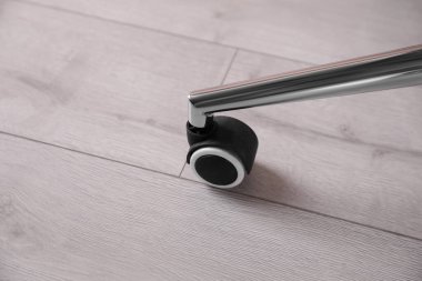 Ahşap zemin üzerinde tekerleği olan modern ofis sandalyesi, yakın plan.