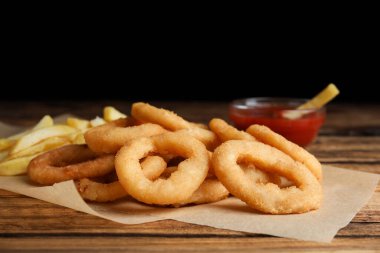 Lezzetli soğan halkaları, patates kızartması ve ketçap ahşap masada, yakın plan.