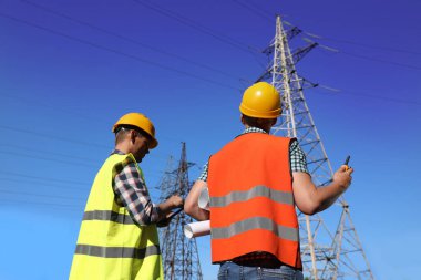 Yüksek voltaj kulelerinin yanında üniformalı profesyonel elektrikçiler.