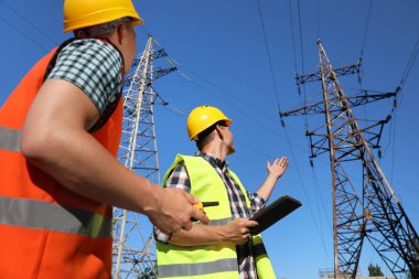 Yüksek voltaj kulelerinin yanında üniformalı profesyonel elektrikçiler.