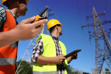 Yüksek voltaj kulelerinin yanındaki profesyonel elektrikçiler, taşınabilir radyo istasyonuna odaklanıyorlar.
