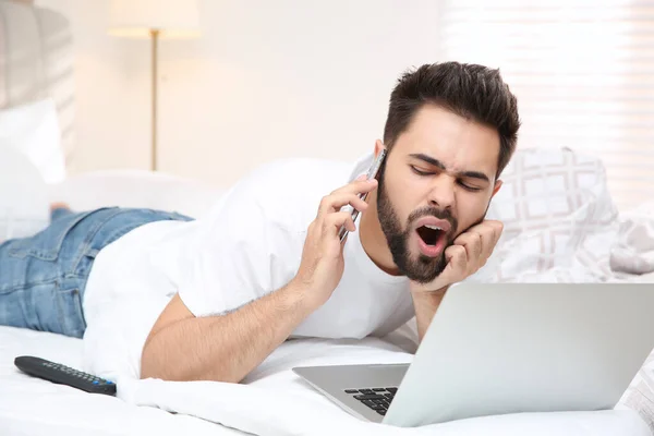 Joven Perezoso Con Portátil Teléfono Inteligente Cama Casa —  Fotos de Stock