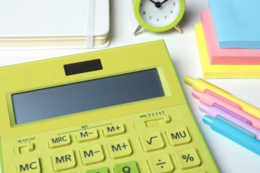 Hesap makinesi, alarm saati ve kırtasiye malzemesi beyaz masada, yakın plan. Vergi muhasebesi