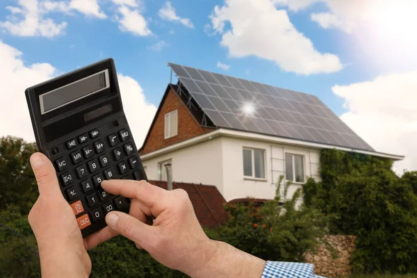 Człowiek Używający Kalkulatora Przeciwko Domowi Zamontowanymi Panelami Słonecznymi Energia Odnawialna — Zdjęcie stockowe