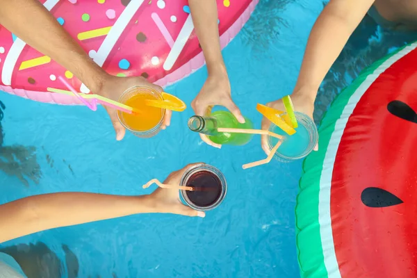 People toasting with refreshing drinks at pool party, top view