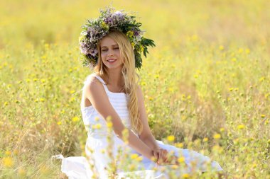 Güneşli bir günde tarlada çiçeklerden yapılmış çelenk giyen genç bir kadın.