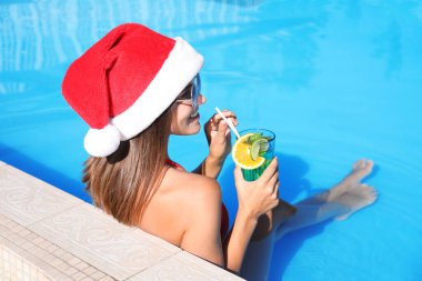 Yüzme havuzunda Noel Baba şapkası takan genç bir kadın. Noel tatili
