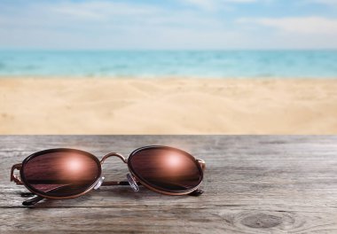 Deniz kenarındaki ahşap masada, kumlu plajda şık güneş gözlükleri.