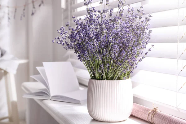 Beautiful lavender flowers and book on window sill indoors