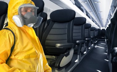 Coronavirus 'un yayılmasını önlemek için uçakta koruyucu elbise giyen bir adam.