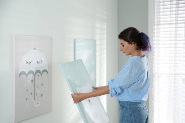 Dekoratör beyaz duvara resim asıyor. Çocuk odası iç tasarımı.