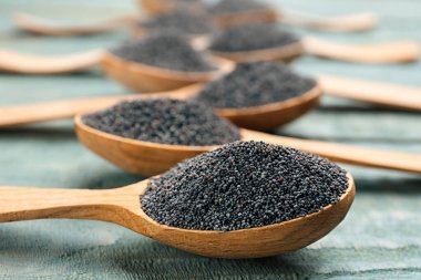 Mavi tahta masadaki kaşıklarda haşhaş tohumları, yakın plan.