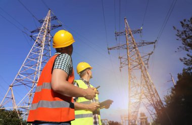 Yüksek voltaj kulelerinin yanında üniformalı profesyonel elektrikçiler.