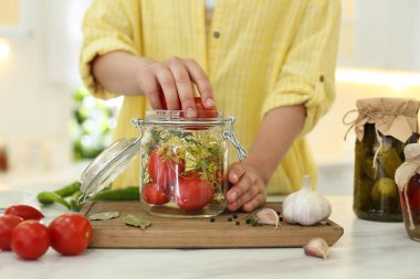 Mutfak masasında domatesleri turşu kavanozuna koyan kadın, yakın plan.