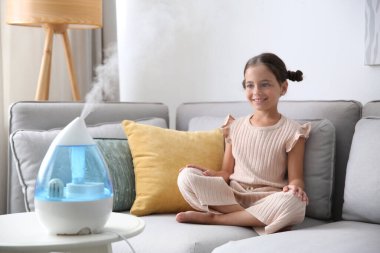 Küçük kız modern hava nemlendiricisi olan bir odada kanepede yatıyor.