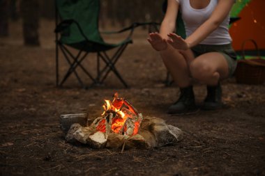 Ormanda yanan odunların yanında elleri ısıtan bir kadın, yakın plan.