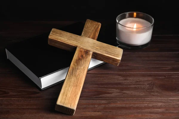 Cross, Bible and burning candle on wooden background, closeup. Christian religion