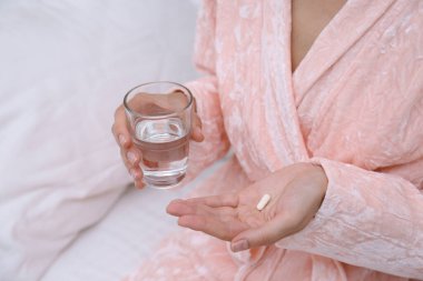 Yatak odasında elinde bir bardak su ve hap tutan kadın, yakın plan.