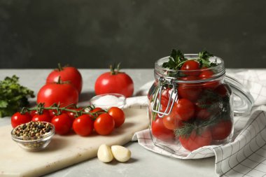 Taze kiraz domatesli turşu kavanozu ve gri masada baharatlar.