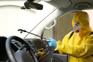 Koruyucu giysili biri arabayı spreyle dezenfekte ediyor. Koronavirüs salgını sırasında önleyici önlemler