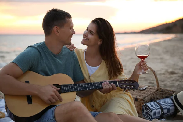 Härligt Par Med Gitarr Och Picknickkorg Stranden Vid Solnedgången — Stockfoto