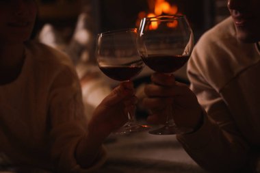 Yanan şöminenin yanında kırmızı şarap bardakları olan çift, yakın plan.