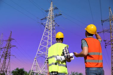 Yüksek voltaj kulelerinin yanında üniformalı profesyonel elektrikçiler.