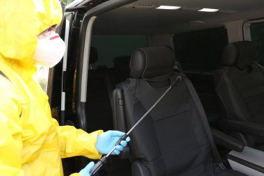 Koruyucu giysili biri arabayı spreyle dezenfekte ediyor. Koronavirüs salgını sırasında önleyici önlemler