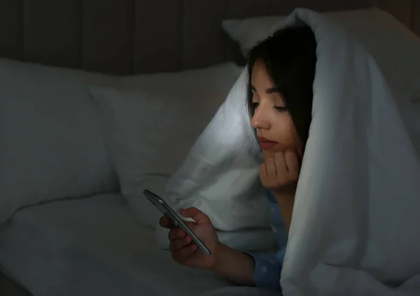 年轻女子在黑暗的卧室里用毛毯下的手机 — 图库照片
