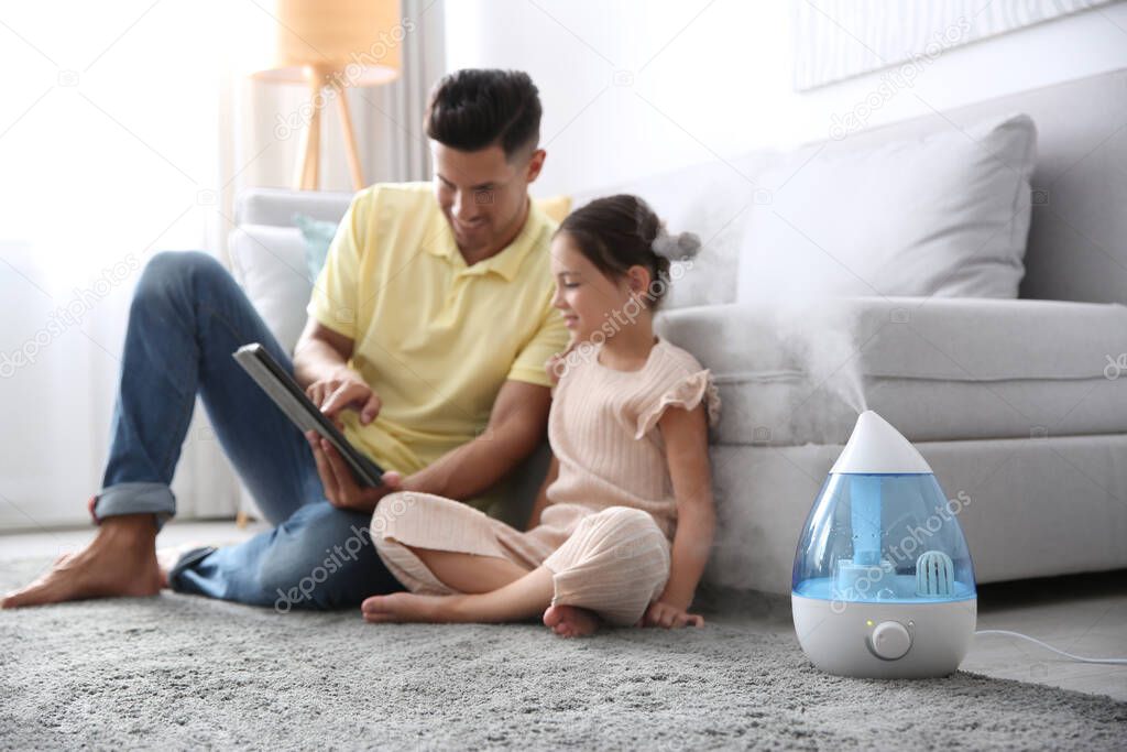 Father and daughter with tablet near modern air humidifier at home