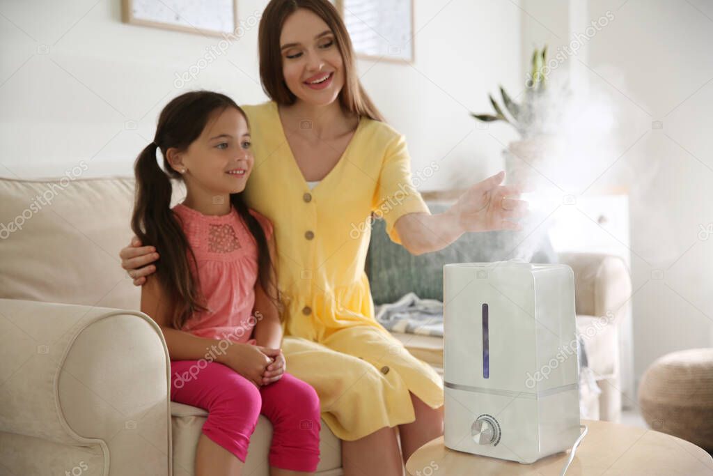 Mother and daughter near modern air humidifier at home