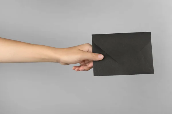 薄い灰色の背景に黒い紙の封筒を持っている女性 クローズアップ — ストック写真