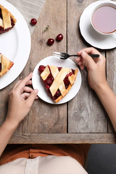 Woman eating delicious cherry pie at wooden table, top view