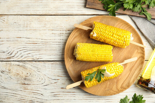 Fresh corn cobs with butter on white wooden table, flat lay. Space for text