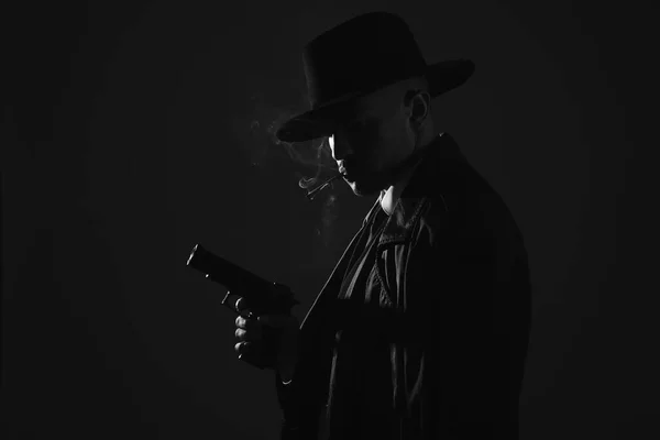 Old fashioned detective with gun smoking cigarette on dark background, black and white effect