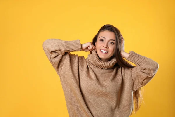 Young woman in stylish brown sweater on yellow background