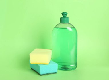 Yeşil arka planda bir şişe deterjan ve sünger.