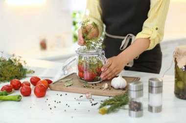 Kadın mutfaktaki masada turşu kavanozuna dereotu koyuyor, yakın plan.