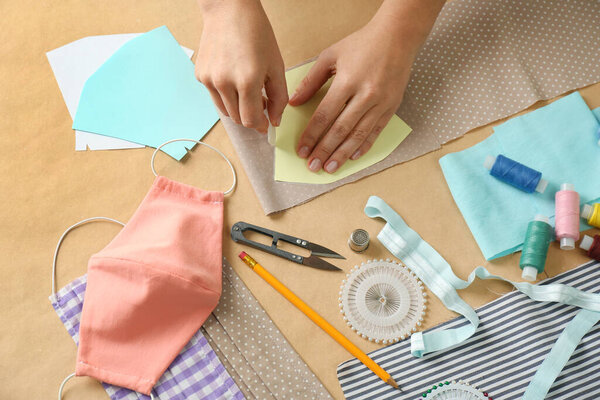 Женщина делает шаблон для шитья ткани маски за столом, крупным планом. Средства индивидуальной защиты во время пандемии COVID-19