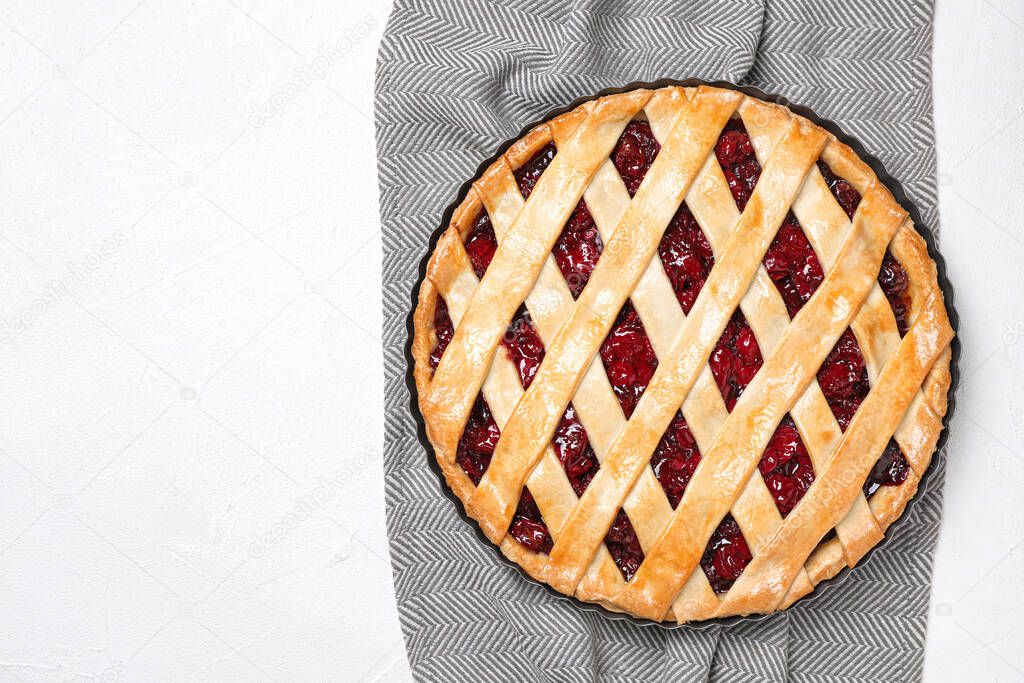 Delicious fresh cherry pie and grey towel on white table, top view. Space for text