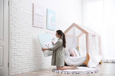 Dekoratör beyaz tuğla duvara resim asıyor. Çocuk odası iç tasarımı.