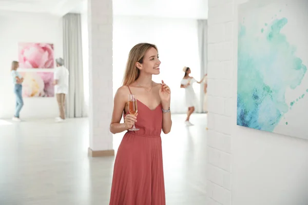 Young woman with glass of champagne at exhibition in art gallery