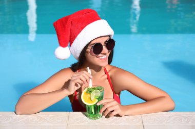 Yüzme havuzunda Noel Baba şapkası takan genç bir kadın. Noel tatili