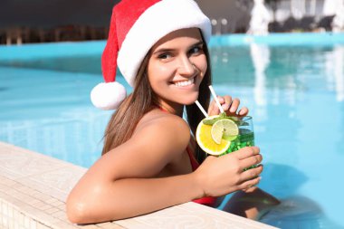 Yüzme havuzunda Noel Baba şapkası takan genç bir kadın. Noel tatili