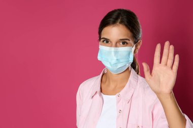 Koruyucu maskeli kadın pembe arka planda merhaba işareti yapıyor, mesaj için yer var. Koronavirüs salgını sırasında sosyal mesafeyi korumak