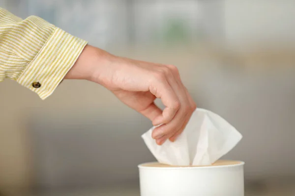 Woman taking paper tissue from holder indoors, closeup
