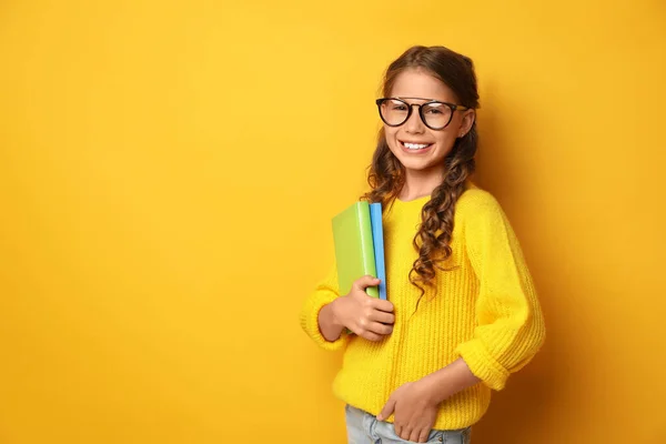 Happy little girl with books on yellow background